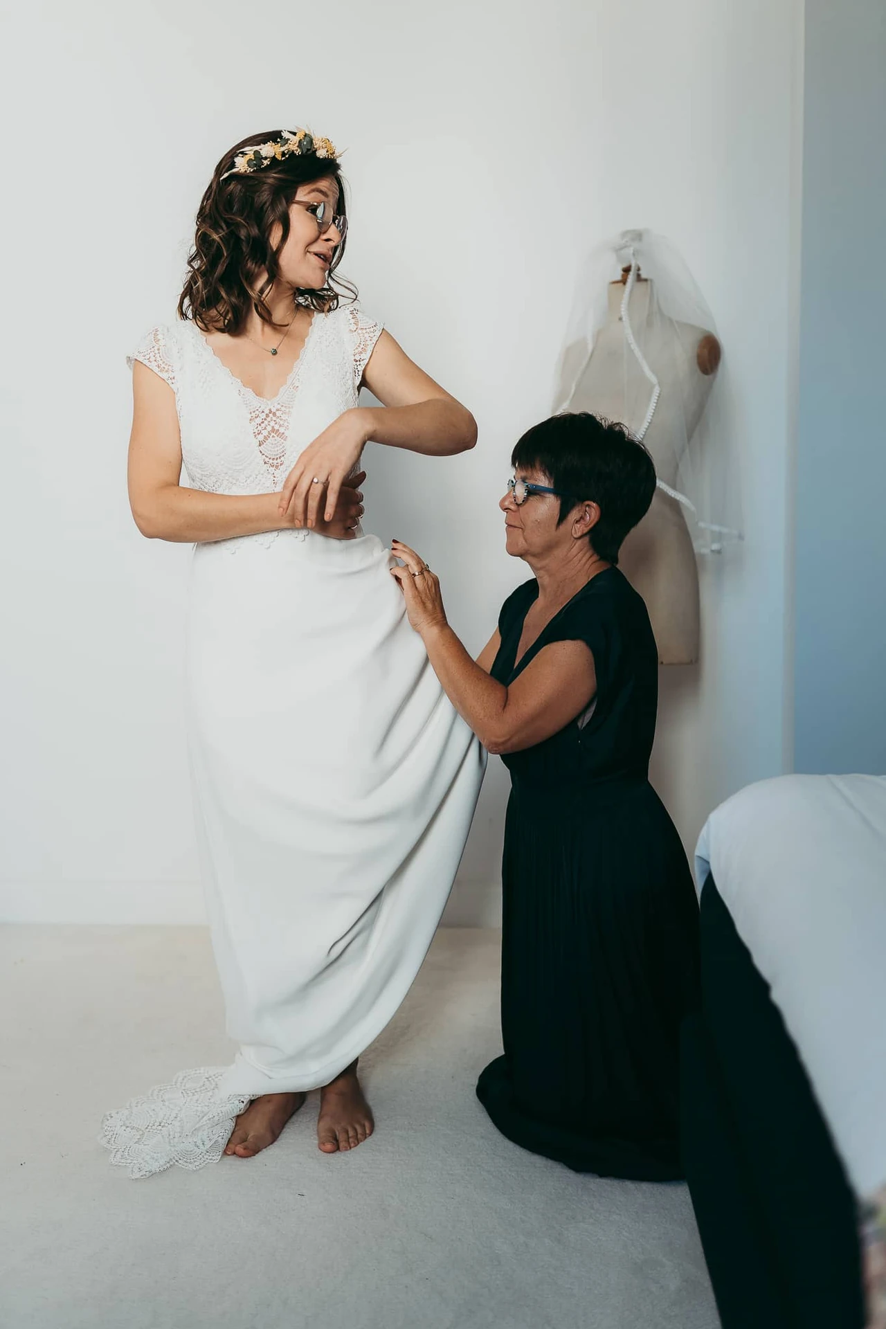 Une proche aide la mariée à ajuster sa robe.