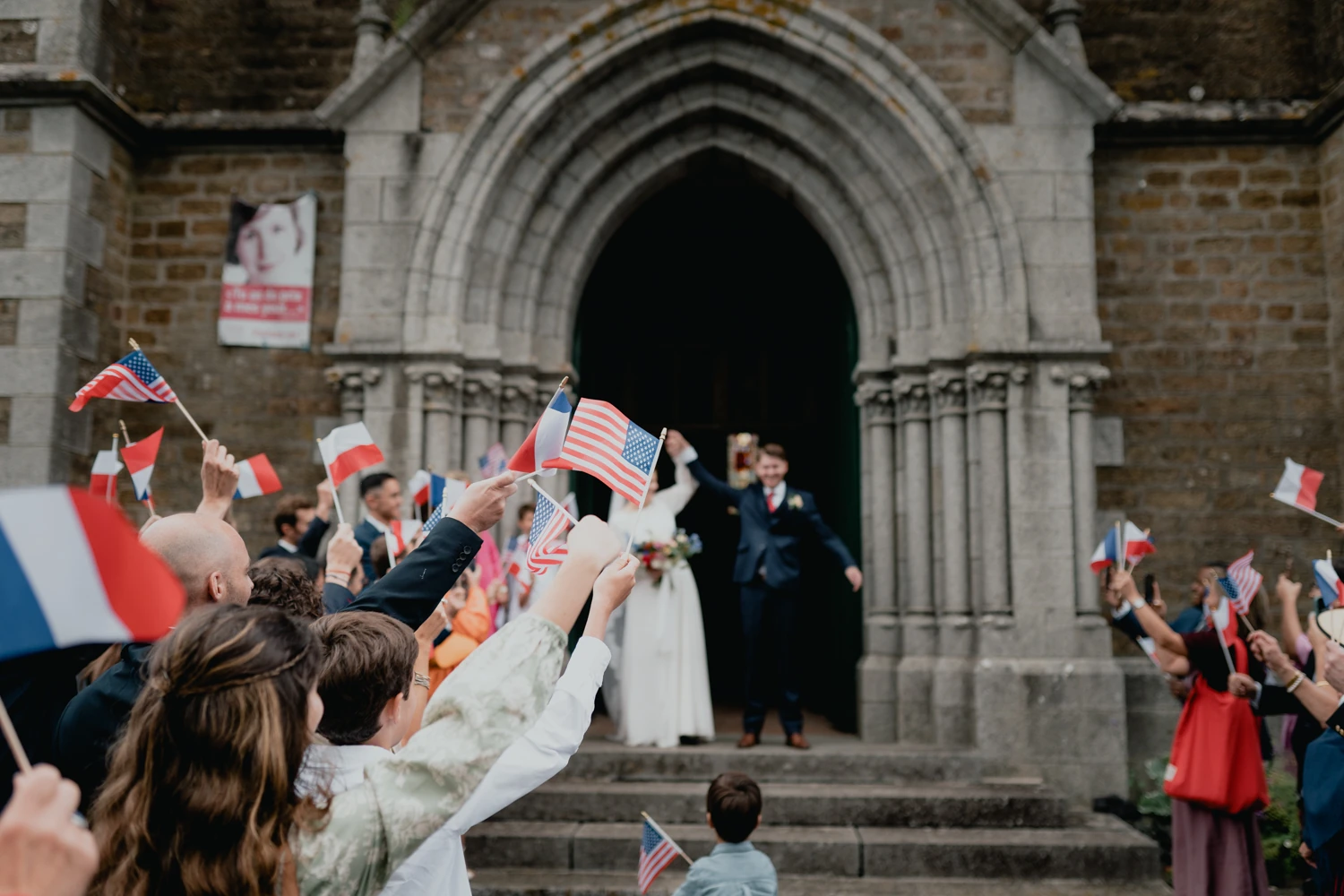 Les invités accueillent les mariés avec des drapeaux à la sortie de l’église.