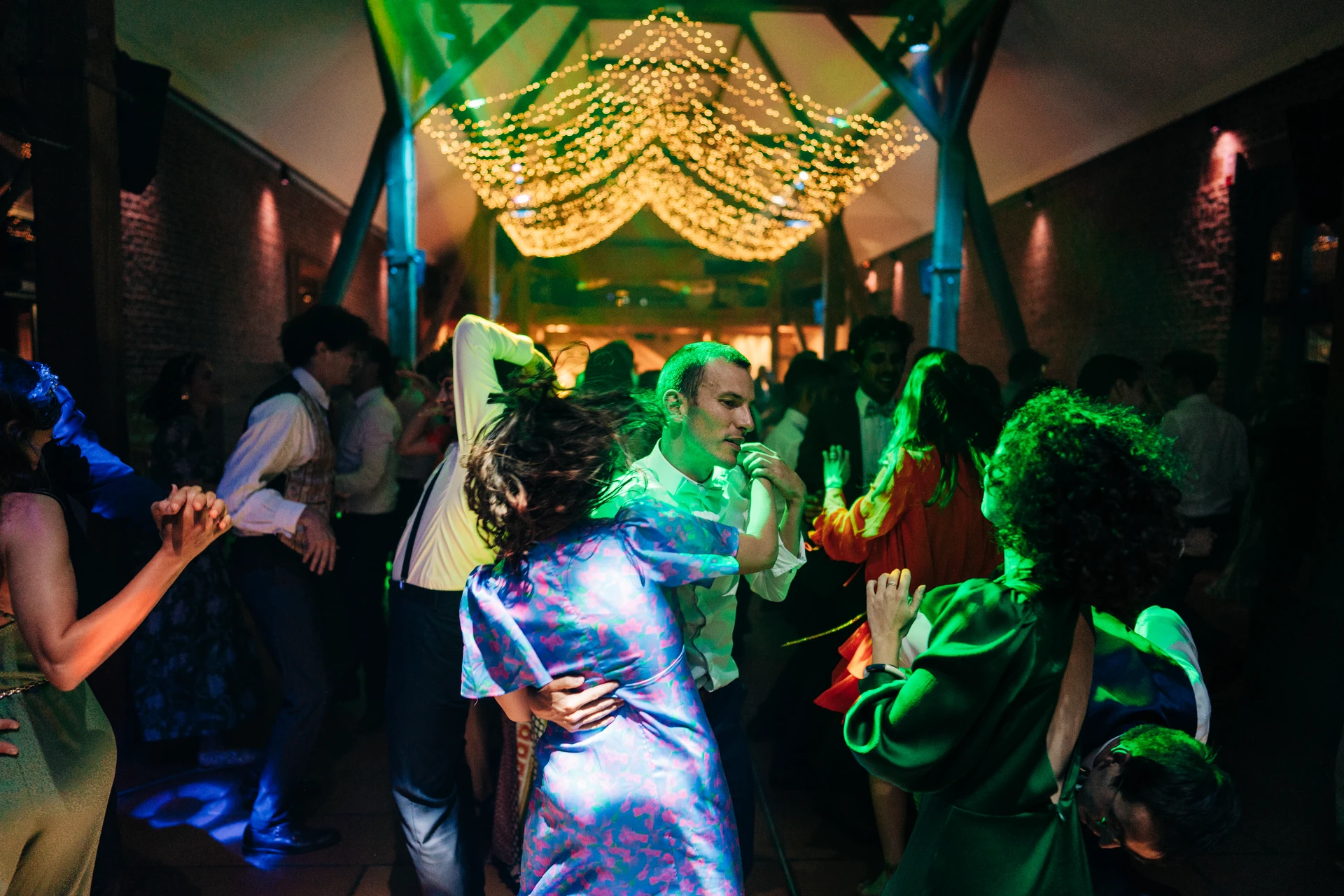 Les mariés et leurs invités dansent sous les lumières colorées de la soirée.