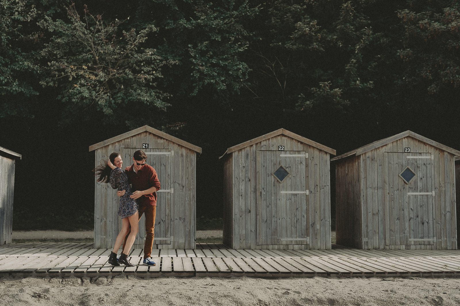 Un couple rit devant des cabines de plage en bois.