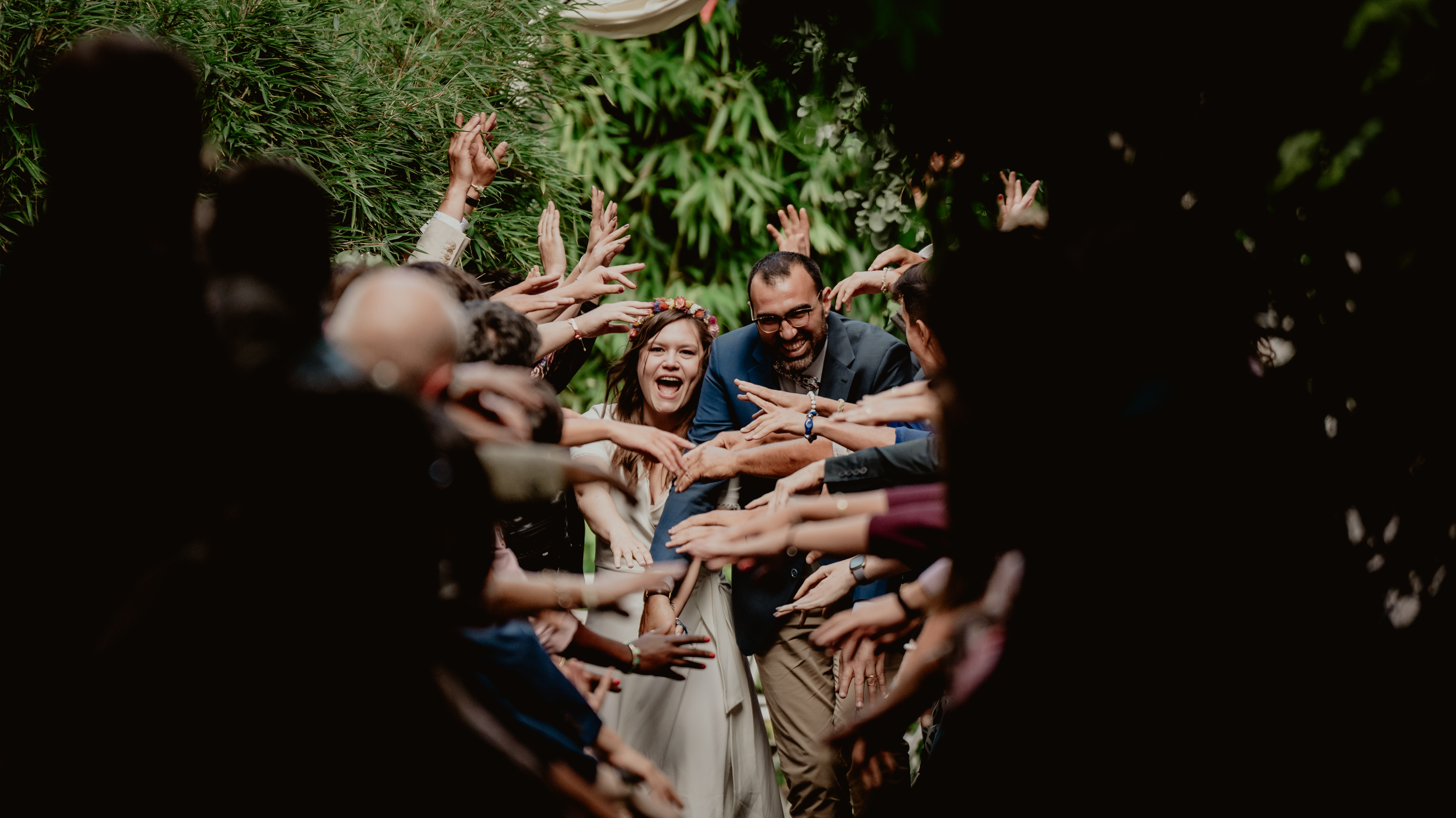 Les mariés sourient sous un tunnel formé par les bras de leurs invités.