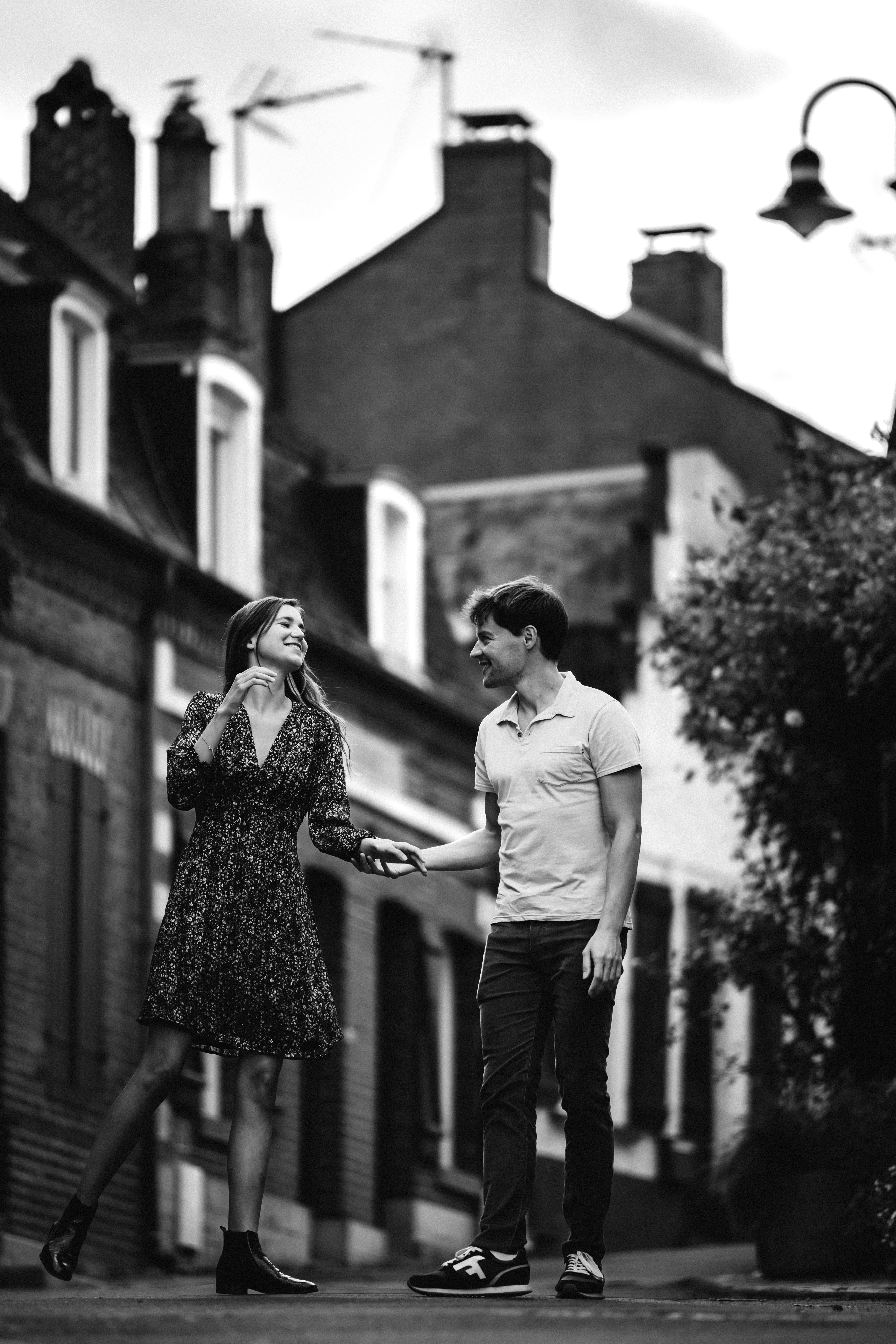 Un couple se tient la main dans une rue pavée, en noir et blanc.
