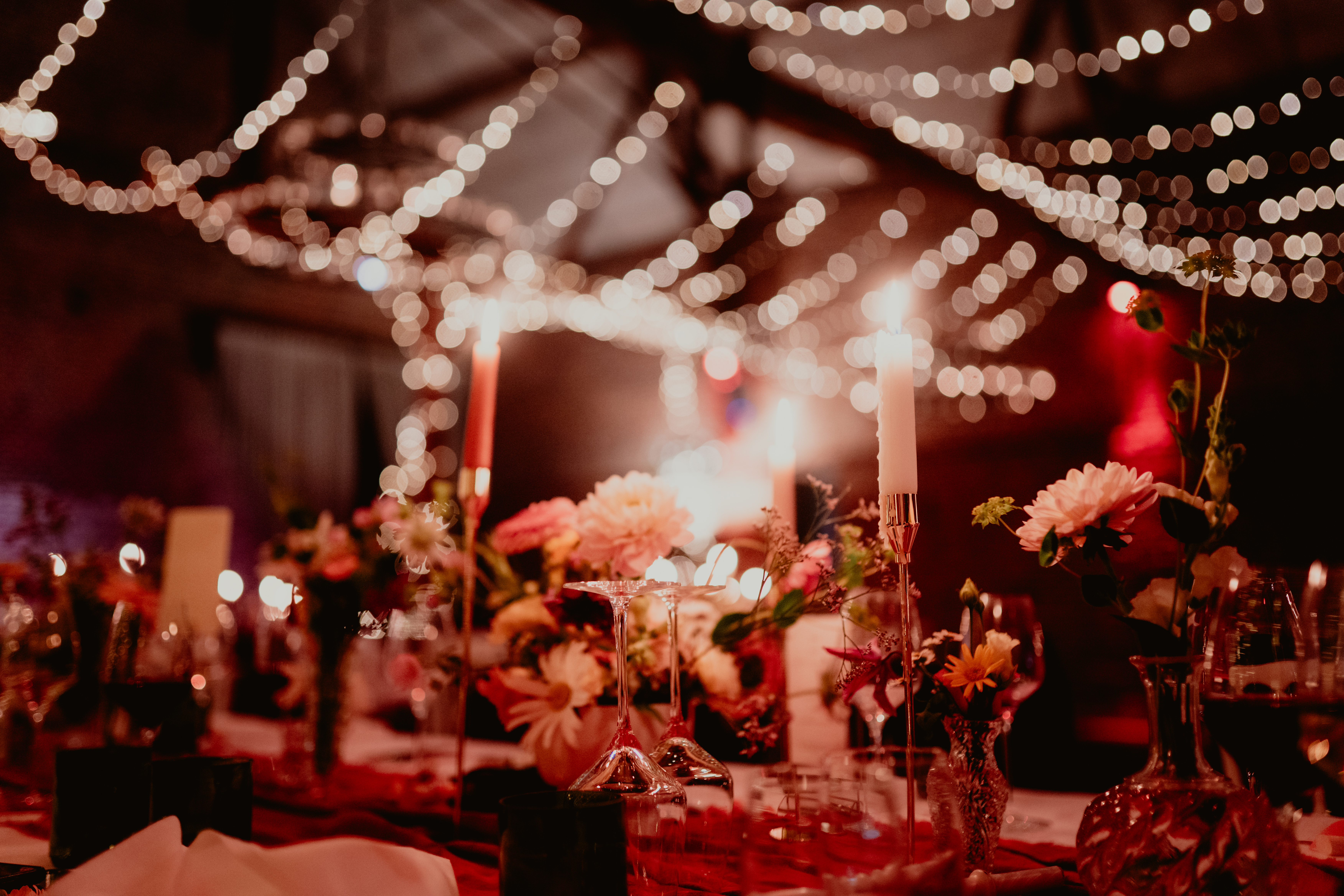 Fleurs et bougies sur une table de réception, sous des guirlandes lumineuses.