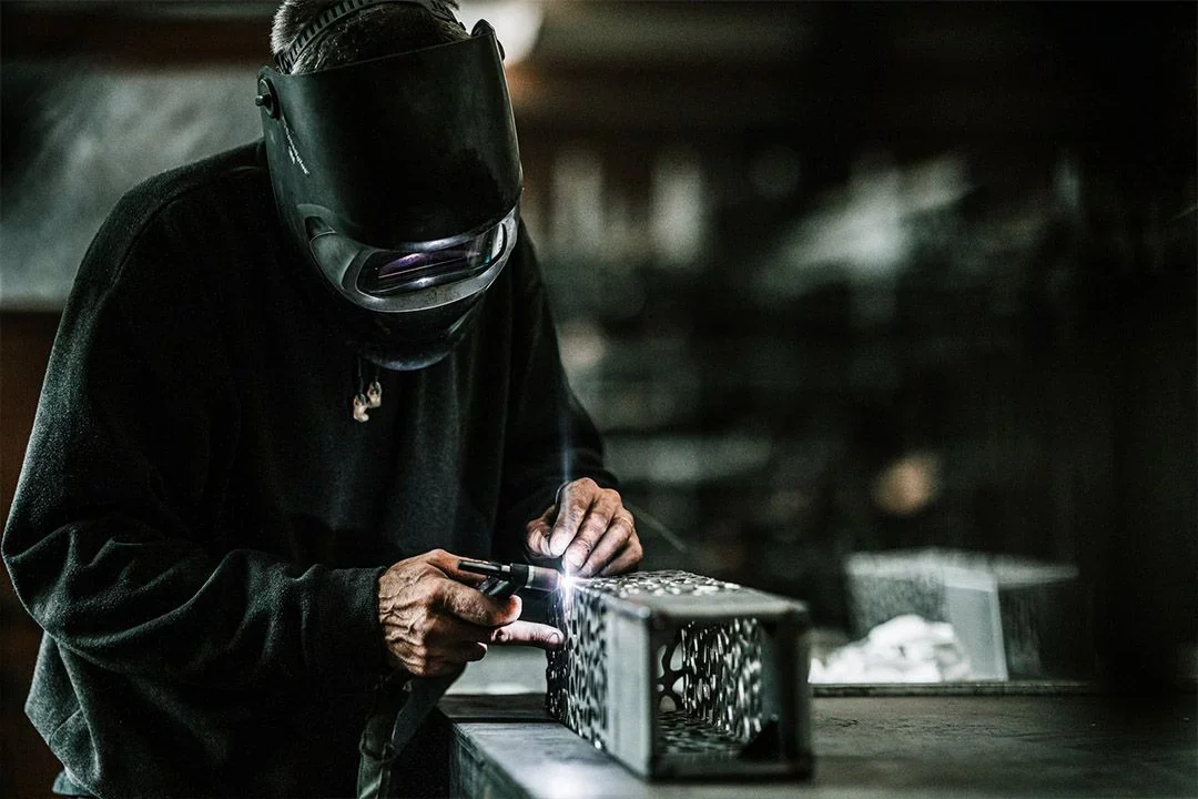 Un artisan soude une pièce dans son atelier, photographié par Sébastien Gras.