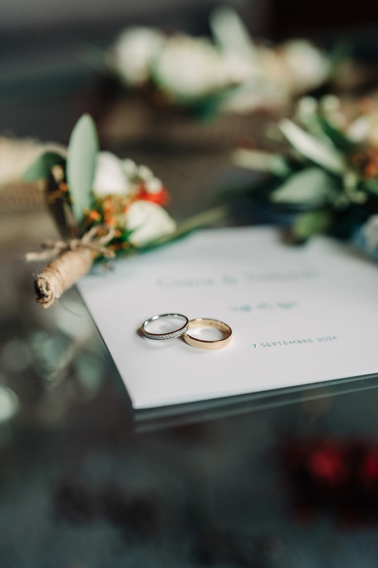 Deux alliances posées sur un faire-part de mariage, entourées de fleurs.
