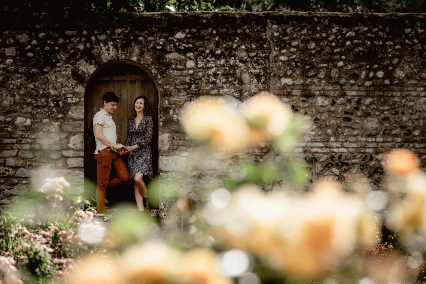 Couple photographié devant une porte en pierre, avec des fleurs au premier plan.